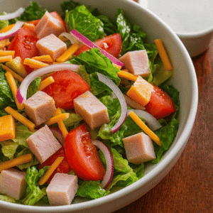 A salad with romaine lettuce, smoked turkey breast, honey ham, cheddar cheese, onions, and tomatoes.