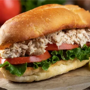 A sandwich with Tuna salad, cheddar cheese, lettuce, tomato, onions, and mayonnaise.